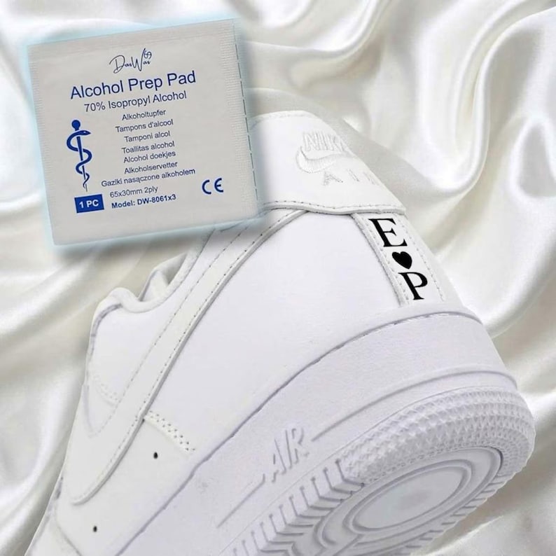May include: White athletic shoe with the letters "EP" and a heart symbol on the heel. An alcohol prep pad is in the background. The prep pad has text that reads "Alcohol Prep Pad" and "70% Isopropyl Alcohol".