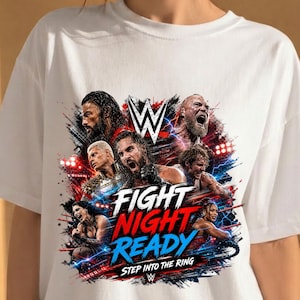 May include: A white t-shirt featuring a graphic print of multiple WWE wrestlers, the WWE logo, and the text "FIGHT NIGHT READY STEP INTO THE RING" in bold white, red, and blue lettering with a distressed, energetic background design.