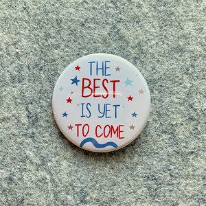 May include: White button with red and blue stars and text that reads "The Best Is Yet To Come".