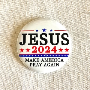 Puede incluir: Un bot&oacute;n blanco con estrellas y rayas rojas, azules y blancas. El bot&oacute;n dice "JESUS 2024" y "MAKE AMERICA PRAY AGAIN".