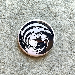 May include: Black and white button featuring a stylized eagle head with a swirling background.