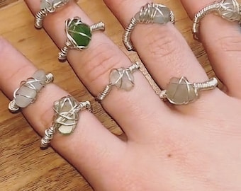 May include: A hand model wearing several silver wire wrapped rings with different colored glass stones. The rings are made with a simple wire wrapping technique and feature a variety of colors and shapes of glass stones.