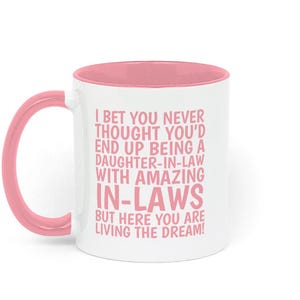May include: A white ceramic mug with a pink interior and a pink handle. The exterior features pink text that reads: I BET YOU NEVER THOUGHT YOU'D END UP BEING A DAUGHTER-IN-LAW WITH AMAZING IN-LAWS BUT HERE YOU ARE LIVING THE DREAM!