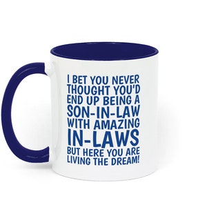 May include: White coffee mug with a blue rim and handle. The mug has a blue inscription that reads: "I bet you never thought you'd end up being a son-in-law with amazing in-laws but here you are living the dream!"