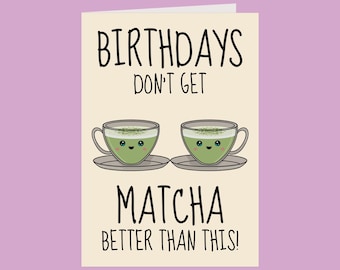 May include: A greeting card with the text "BIRTHDAYS DON'T GET MATCHA BETTER THAN THIS!". The card features two cartoon matcha tea cups with smiling faces, each on a saucer. The background is a light beige color, with a purple background.