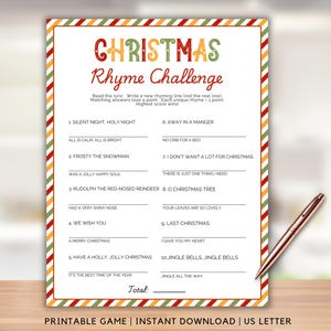 May include: A printable Christmas Rhyme Challenge game on US Letter paper. The game features a festive design with a red, green, and yellow striped border. A rose gold pen rests on the wooden surface next to the game.