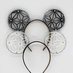 May include: Two headbands featuring circular ears with geometric lattice patterns. One headband has black ears, the other has white ears. Each circular ear is bordered by a row of small, iridescent, light-reflecting crystals that shimmer.