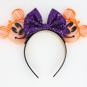 May include: Purple sequined bow headband with orange and black pumpkin Mickey Mouse ears.