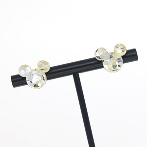 May include: A pair of gold and silver Mickey Mouse head earrings on a black stand.
