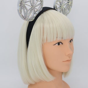 May include: A silver headband with two large, round, sparkly, geometric-shaped ears. The headband is black and the ears are decorated with iridescent rhinestones.