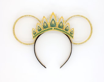 May include: Gold crown headband with green and white accents and rhinestones. The headband is shaped like Mickey Mouse ears.