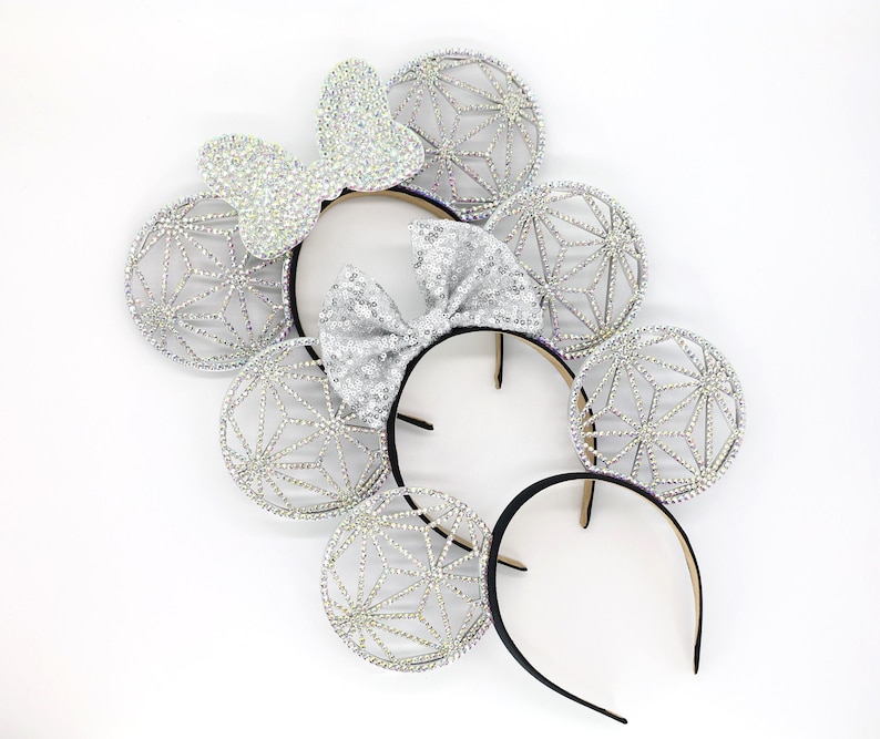 May include: Silver sparkly headband with a bow and three pairs of sparkly ears. Each ear is a geometric design.
