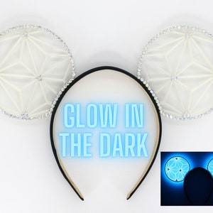 May include: White glow-in-the-dark Mickey Mouse ears with a geometric design and rhinestones. The ears glow blue in the dark.