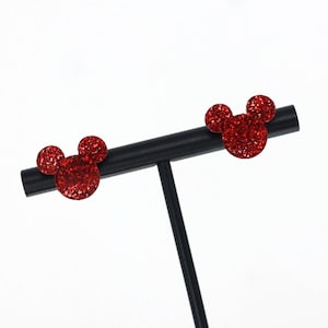 May include: A pair of red glitter Mickey Mouse earrings on a black earring stand.
