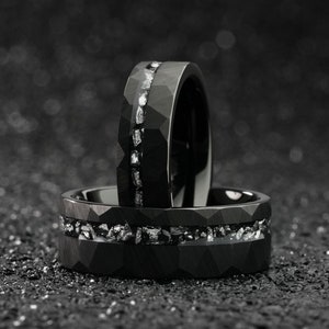 K&ouml;nnte beinhalten: Zwei schwarze Ringe aus Wolframcarbid mit einer Reihe kleiner Diamanten, die in die Band eingefasst sind. Die Ringe sind &uuml;bereinander gestapelt.