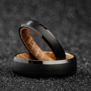 May include: Two black tungsten carbide rings with a wood inlay. The rings are stacked on top of each other.
