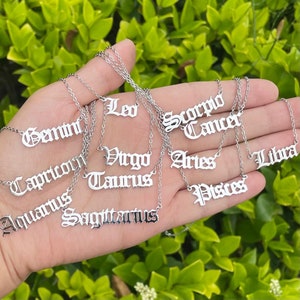 May include: A set of 12 silver necklaces with zodiac signs in a gothic font. The signs are: Gemini, Capricorn, Aquarius, Sagittarius, Leo, Virgo, Taurus, Scorpio, Cancer, Aries, Libra, and Pisces.