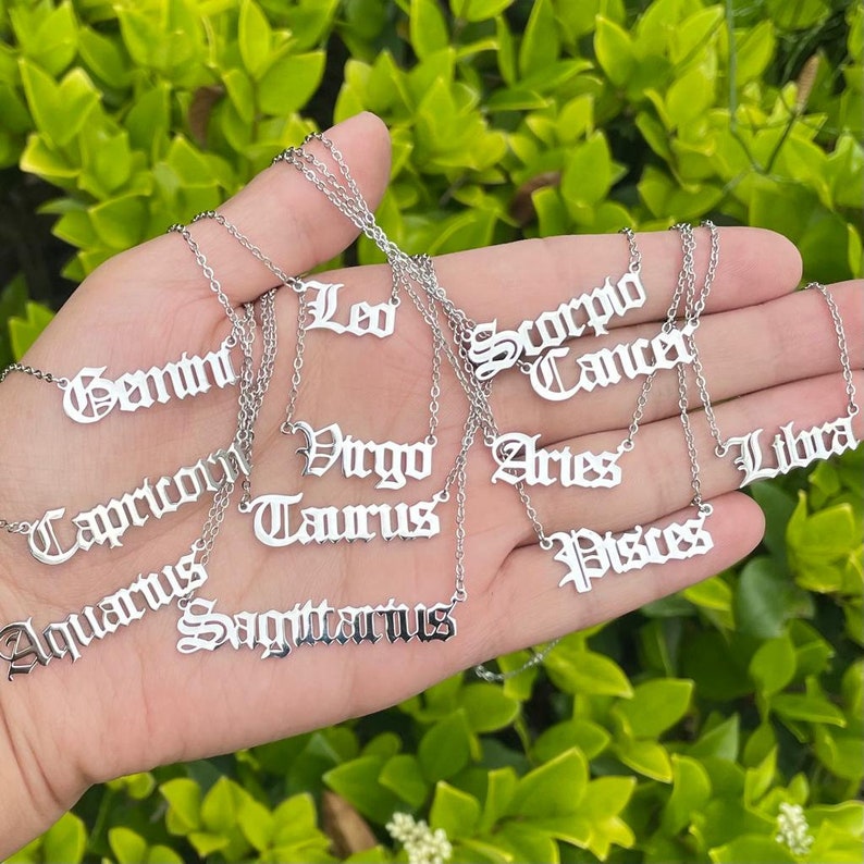 May include: A set of 12 silver necklaces with zodiac signs in a gothic font. The signs are: Gemini, Capricorn, Aquarius, Sagittarius, Leo, Virgo, Taurus, Scorpio, Cancer, Aries, Libra, and Pisces.