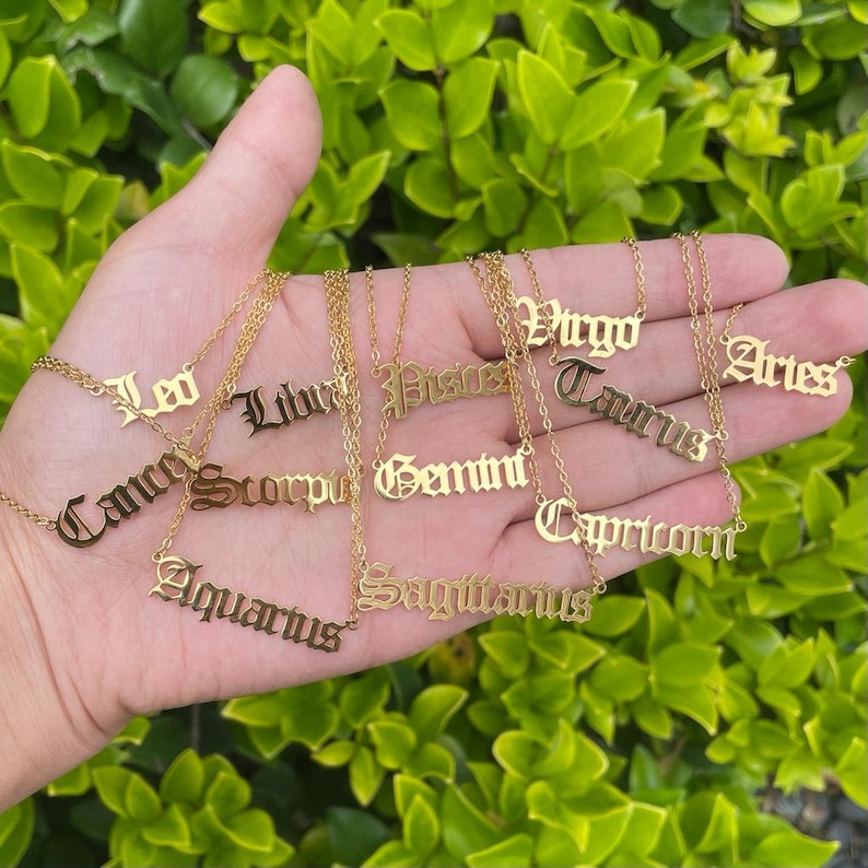 May include: A collection of gold necklaces with zodiac signs in a gothic font. The signs include Aries, Taurus, Gemini, Cancer, Leo, Virgo, Libra, Scorpio, Sagittarius, Capricorn, Aquarius, and Pisces.