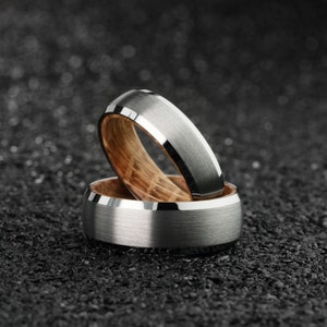 K&ouml;nnte beinhalten: Zwei silberne und h&ouml;lzerne Ringe, die &uuml;bereinander gestapelt sind. Der obere Ring ist ein silbernes Band mit einer abgeschr&auml;gten Kante. Der untere Ring ist ein silbernes Band mit einer Holzeinlage.