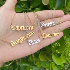 May include: Five gold and silver necklaces with zodiac signs in a gothic font. The signs are Capricorn, Sagittarius, Aries, Gemini, and Aquarius.