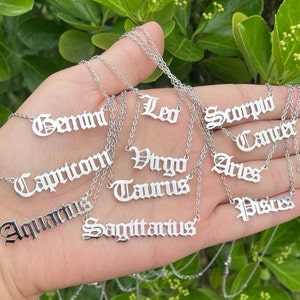 May include: A set of twelve silver necklaces with zodiac signs written in an old English font. The signs include Gemini, Leo, Scorpio, Cancer, Capricorn, Virgo, Aries, Taurus, Aquarius, Sagittarius, and Pisces.