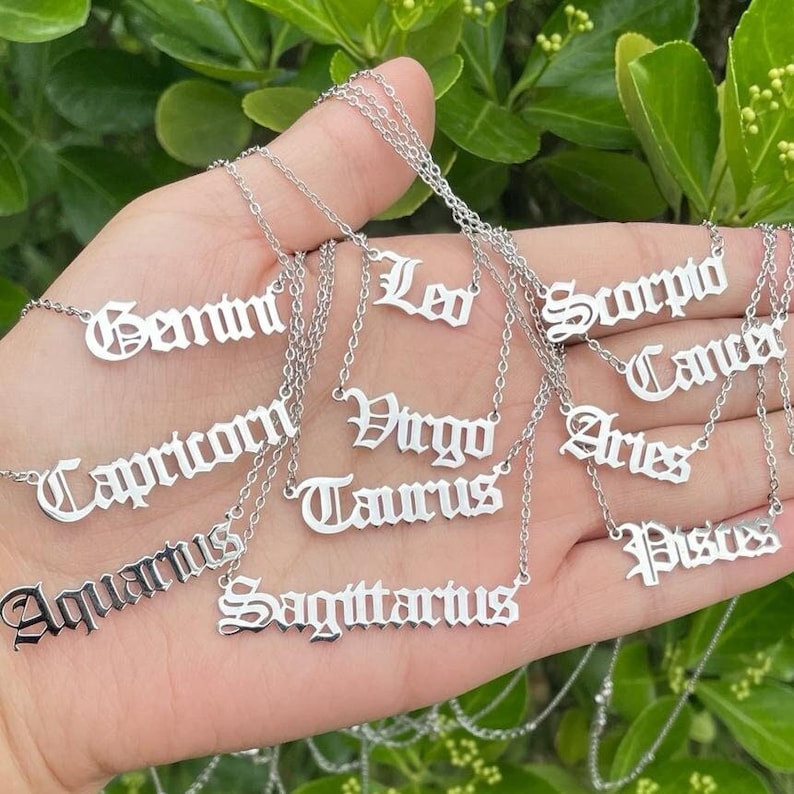 May include: A set of twelve silver necklaces with zodiac signs written in an old English font. The signs include Gemini, Leo, Scorpio, Cancer, Capricorn, Virgo, Aries, Taurus, Aquarius, Sagittarius, and Pisces.