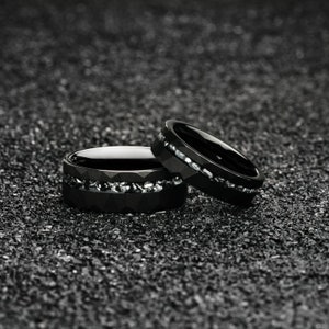 K&ouml;nnte beinhalten: Zwei schwarze Ringe aus Wolframcarbid mit einem silbernen Band aus kleinen Steinen am Rand.