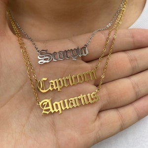 May include: Three gold necklaces with zodiac signs. The top necklace has the word "Scorpio" in silver. The middle necklace has the word "Capricorn" and the bottom necklace has the word "Aquarius".