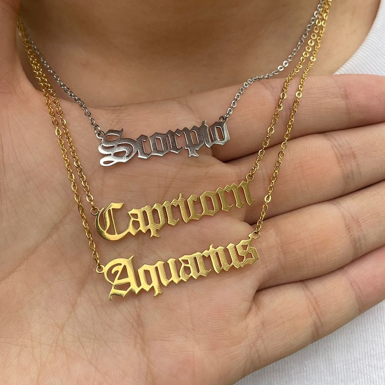 May include: Three gold necklaces with zodiac signs. The top necklace has the word "Scorpio" in silver. The middle necklace has the word "Capricorn" and the bottom necklace has the word "Aquarius".