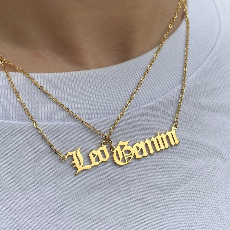 May include: Two gold necklaces with the words "Leo Gemini" in a gothic font.