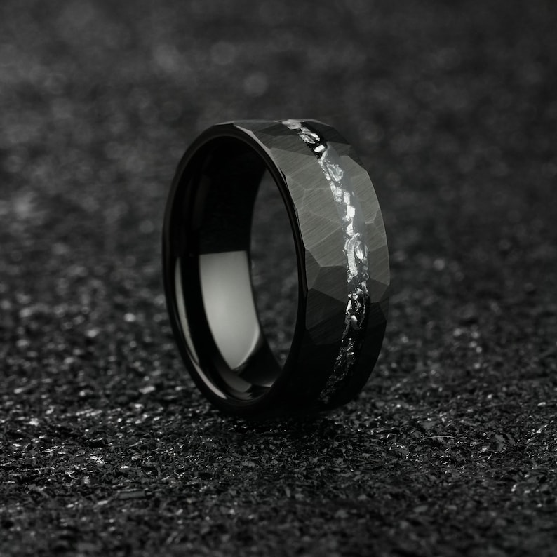 K&ouml;nnte beinhalten: Ein schwarzer Ring aus Wolframcarbid mit geh&auml;mmerter Oberfl&auml;che und einer silbernen Einlage. Der Ring hat ein breites Band und eine bequeme Passform.