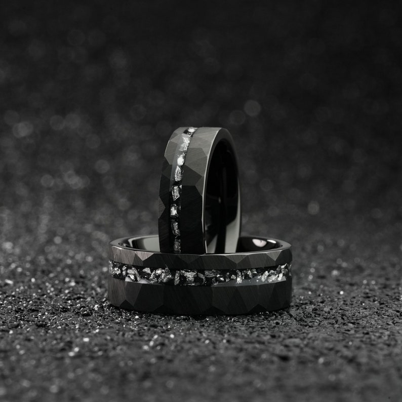 K&ouml;nnte beinhalten: Zwei schwarze Ringe aus Wolframcarbid mit einer Reihe kleiner Diamanten, die in die Band eingefasst sind. Die Ringe sind &uuml;bereinander gestapelt.