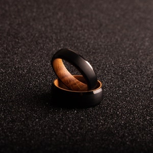 May include: Two black and brown rings stacked on top of each other. The top ring is black with a polished finish and the bottom ring is brown wood with a black inlay.