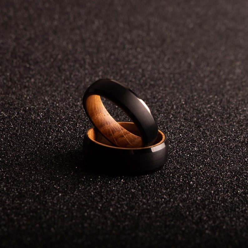 May include: Two black and brown rings stacked on top of each other. The top ring is black with a polished finish and the bottom ring is brown wood with a black inlay.