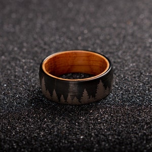 May include: A black tungsten carbide ring with a wood inlay and a design of trees etched into the surface.