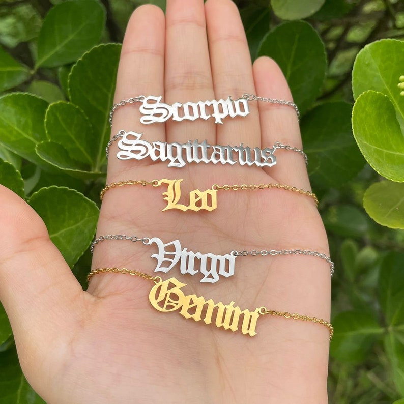 May include: Five gold and silver necklaces with zodiac signs in a gothic font. The signs are Scorpio, Sagittarius, Leo, Virgo, and Gemini.