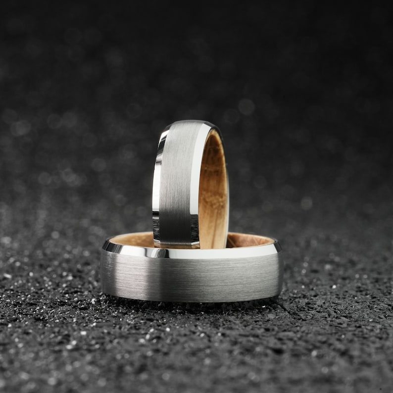 K&ouml;nnte beinhalten: Zwei silberne Eheringe mit geb&uuml;rsteter Oberfl&auml;che. Der obere Ring hat eine Holzeinlage.