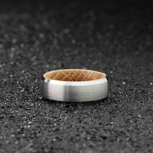 K&ouml;nnte beinhalten: Ein silberner und h&ouml;lzerner Ring mit geb&uuml;rsteter Oberfl&auml;che. Der Ring hat einen d&uuml;nnen Holzstreifen um die Mitte.