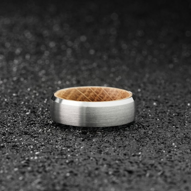 K&ouml;nnte beinhalten: Ein silberner und h&ouml;lzerner Ring mit geb&uuml;rsteter Oberfl&auml;che. Der Ring hat einen d&uuml;nnen Holzstreifen um die Mitte.
