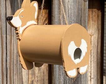 May include: A brown and white wooden birdhouse shaped like a corgi dog. The birdhouse has a round hole for birds to enter and a small opening on the side for cleaning.