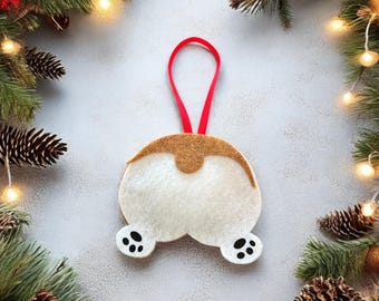 May include: A felt Christmas ornament shaped like a dog's rear end with a red ribbon for hanging. The ornament is white with brown accents and black paw prints.