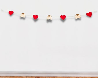 May include: A red heart garland with white string and wooden car cutouts. The garland is hanging on a white wall above a wooden floor.
