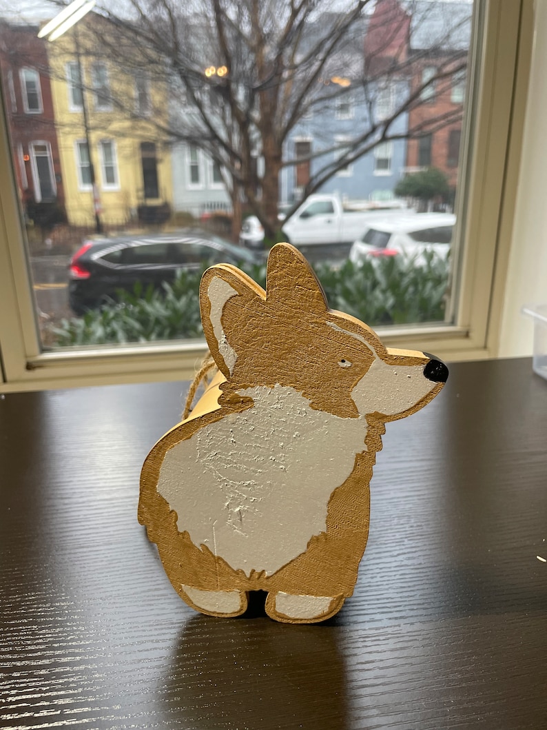 May include: A wooden figurine of a corgi dog painted in gold and white. The dog is standing on its hind legs with its tail curled up.
