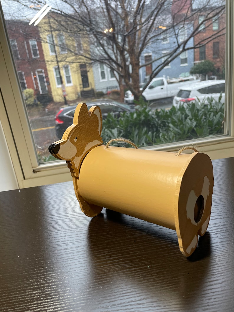 May include: A wooden, hand-painted, brown and white corgi dog shaped birdhouse with a hole in the back for birds to enter.