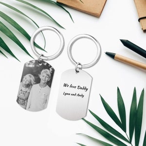 Könnte beinhalten: Zwei silberne Schlüsselanhänger mit einem Schwarzweißfoto von zwei Kindern auf einem Schlüsselanhänger und dem Text "We love Daddy Lynn and Andy" auf dem anderen Schlüsselanhänger.