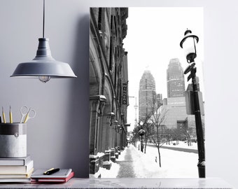 Puede incluir: Fotografía en blanco y negro de una calle de la ciudad en invierno. La calle está bordeada de edificios y una farola. La calle está cubierta de nieve.