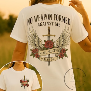 Könnte beinhalten: Weißes T-Shirt mit einem grafischen Design eines Schwertes mit Flügeln und einer Rose. Der Text "No weapon formed against me shall prosper Isaiah 54:17" ist auf dem T-Shirt aufgedruckt.