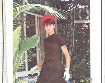 May include: Vogue Paris Original pattern 1605 by Balmain for a dress with a red hat. The model is wearing a brown dress with a belt and white gloves. The dress has short sleeves and a round neckline.