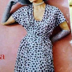 Può includere: Una donna indossa un abito bianco con pois neri e un cappello bianco con un bordo nero. Indossa guanti bianchi e una collana di perle.